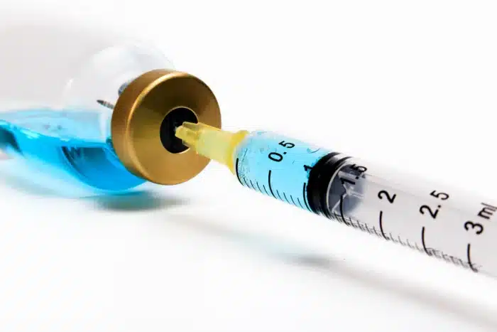 A close-up of a syringe being filled with a blue liquid from a glass vial with a golden cap. The syringe's measurement markings are clearly visible, indicating it can hold up to 3 milliliters of liquid. The background is plain white.