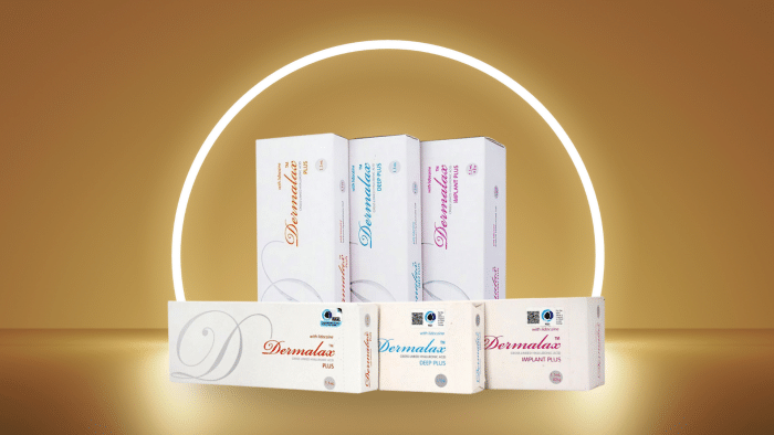 The image shows five boxes of Dermalax products arranged in a row, with three larger boxes standing upright behind two smaller boxes lying flat. The background features a warm, golden gradient with a glowing ring, creating an elegant and premium aesthetic. Wondering what is Dermalax filler?