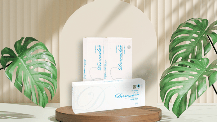 Two Dermalax Deep Plus boxes are displayed, with one standing and one lying on a wooden surface. The backdrop features a beige arch and vertical lines, flanked by large green Monstera leaves casting shadows, creating a natural and serene presentation that mirrors glowing Dermalax Deep Plus reviews.