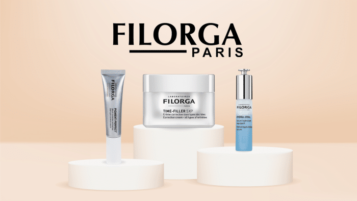 The image showcases three skincare products from Filorga Paris, renowned for their best sellers, placed on separate white stands. From left to right, there's a tube, a jar labeled "Time-Filler 5XP," and a pump bottle. The background is a gradient of light peach, with “Filorga Paris” displayed prominently above the products.