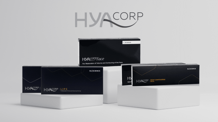The image shows HYAcorp product packaging on display, including boxes for facial restoration, body contouring, and lip augmentation products. The sleek and minimalistic packaging in black and white with silver accents hints at the premium quality one would expect given the hyacorp filler price.