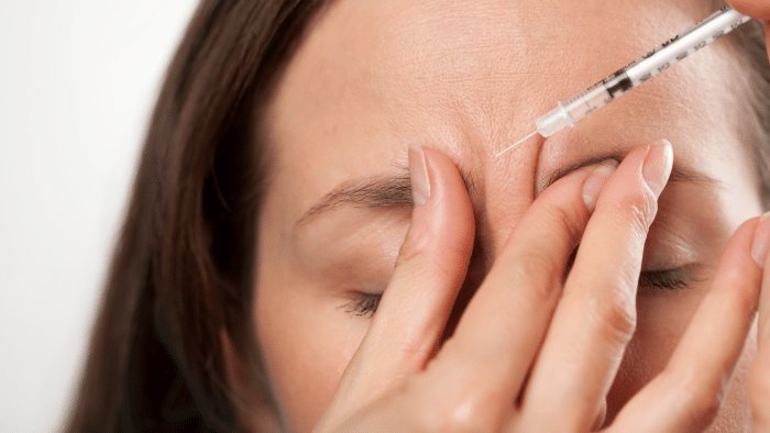 A close-up of a woman with closed eyes receiving a cosmetic injection in the forehead. One hand gently holds the skin while the other administers the syringe, addressing frown lines. For those curious about botox questions and answers, this image highlights the precision involved in the process.