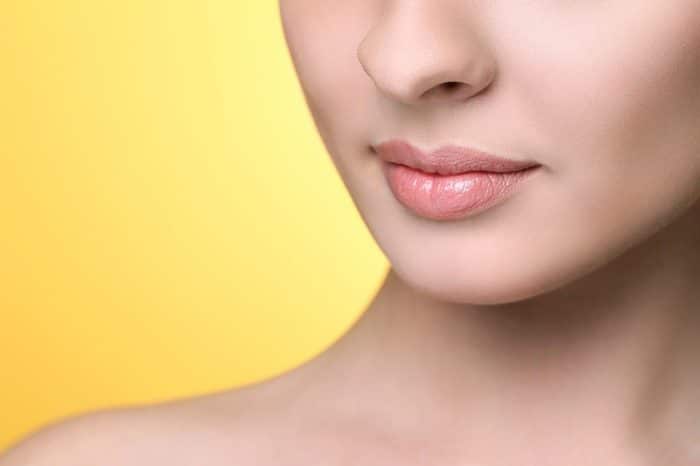 Close-up image of a person's lower face, showcasing smooth, fair skin with a focus on well-defined lips—possibly enhanced by Dysport for lip flip. The background is a solid, vibrant yellow. The person’s shoulders and part of the neck are visible, but the rest of the face is not shown.