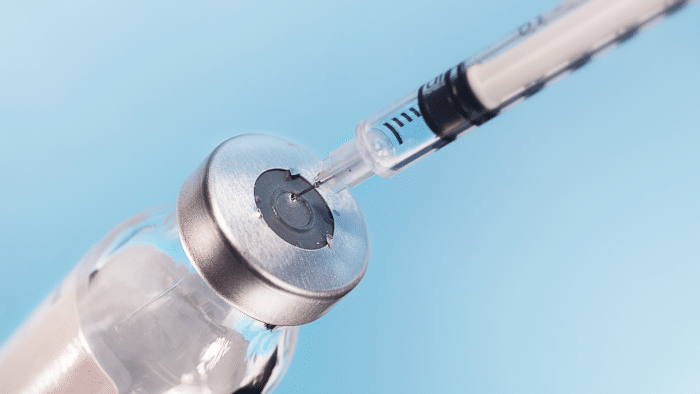 Close-up of a syringe inserting into a vial with a metal cap. The background is a soft blue gradient, suggesting a clinical or medical setting, much like those used in orthovisc vs euflexxa treatments.