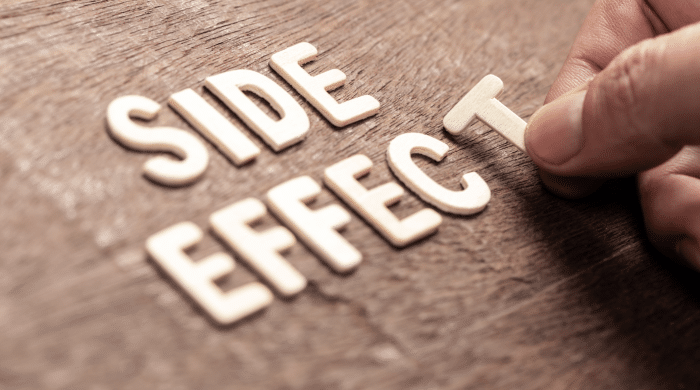 A hand is placing the letter "T" to complete the phrase "SIDE EFFECT" formed from wooden letters on a textured wooden surface.