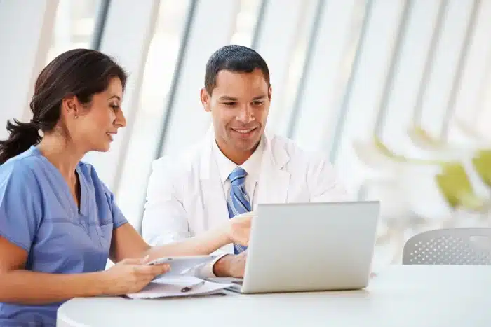 Two medical professionals sitting at the desk and looking together at a laptop screen
