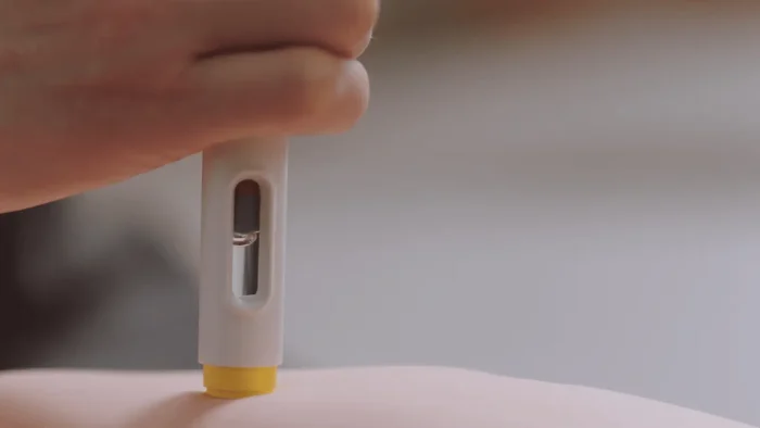 A close-up of a hand holding an epinephrine auto-injector, pressing it against the skin of an arm, ready to administer medication.